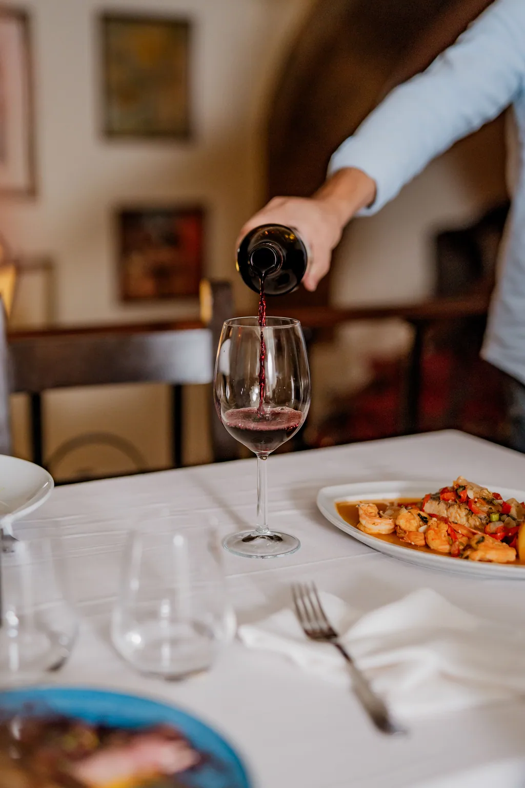 Rotwein wird ins Glas geschenkt, Garnelen auf dem Tisch