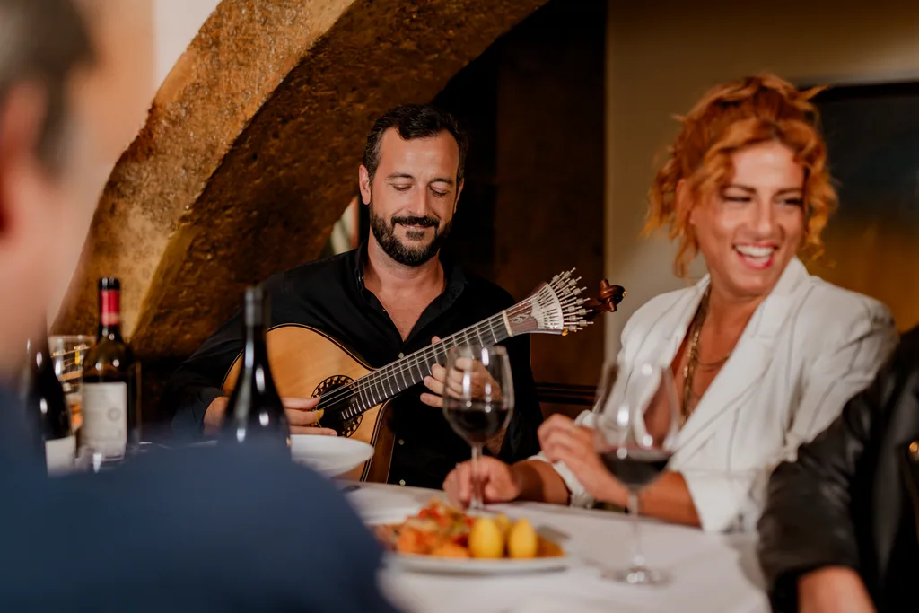 O guitarrista a tocar encostado à mesa, a fadista ao lado