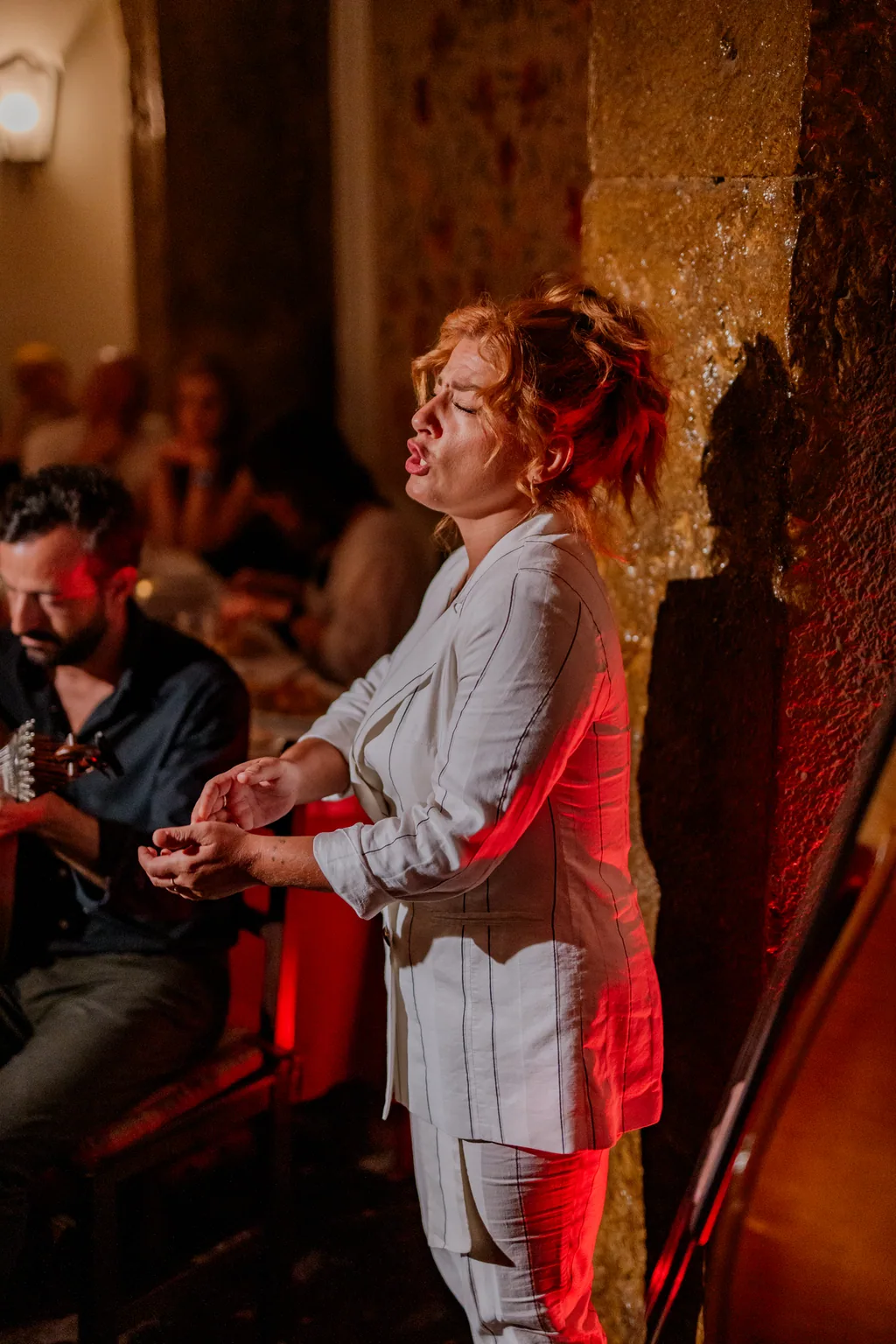 Fado singer performing before the guitarist, red light on the wall
