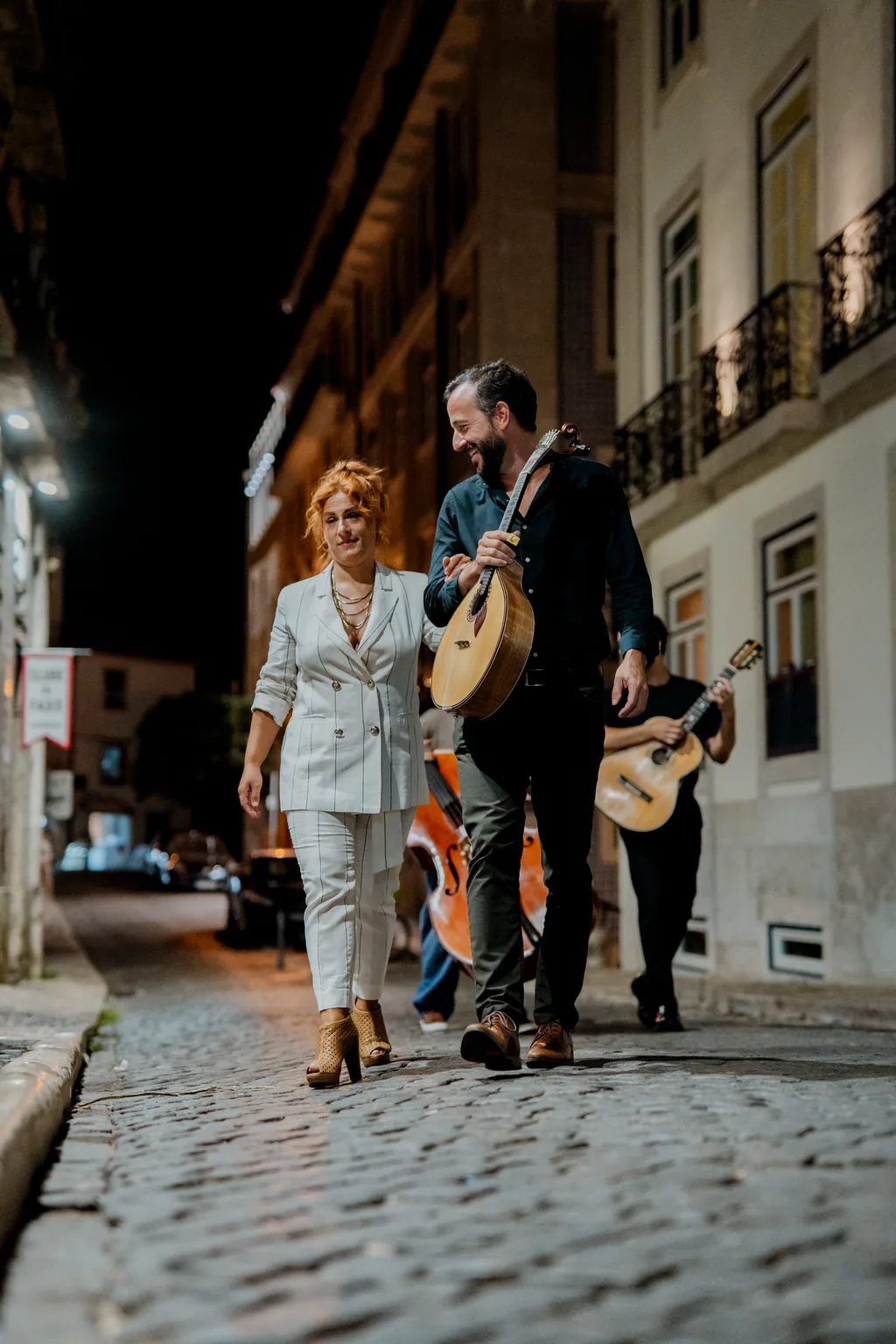 Fadista e dois músicos a subir a calçada de Alfama, à noite