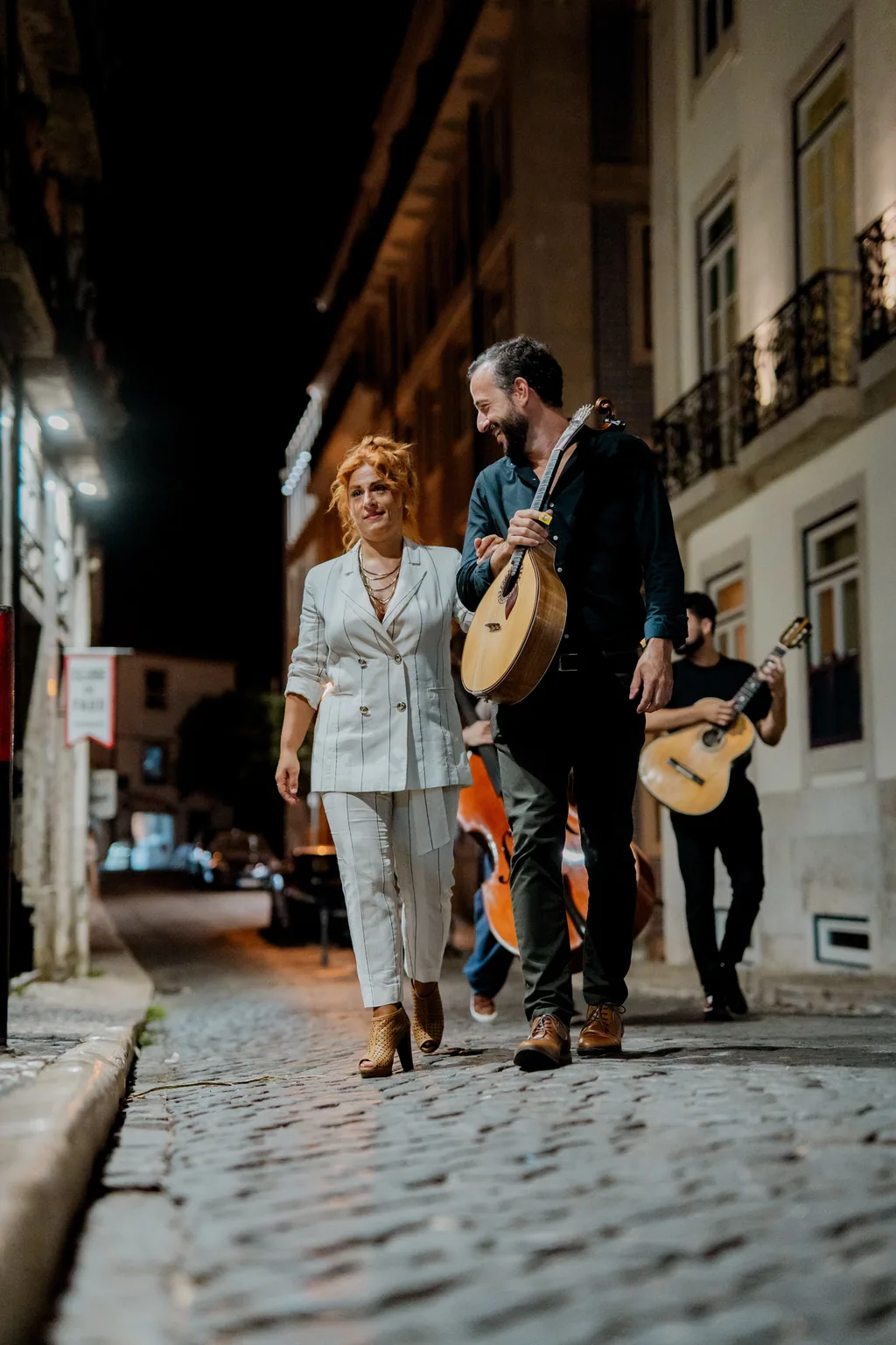 Fado-Sängerin und Gitarristen gehen nachts durch Alfama