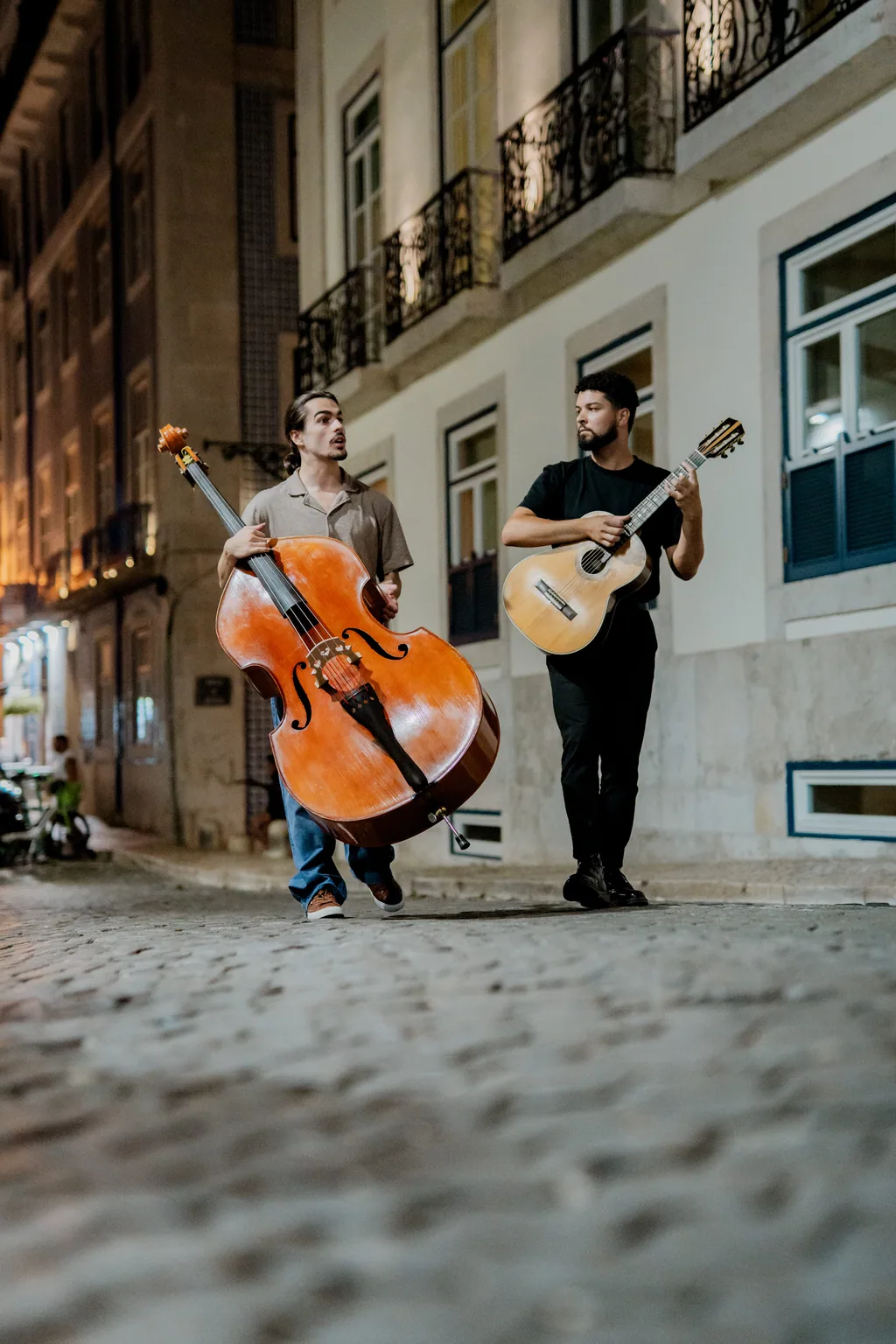 Zwei Musiker tragen Kontrabass und Gitarre übers Pflaster