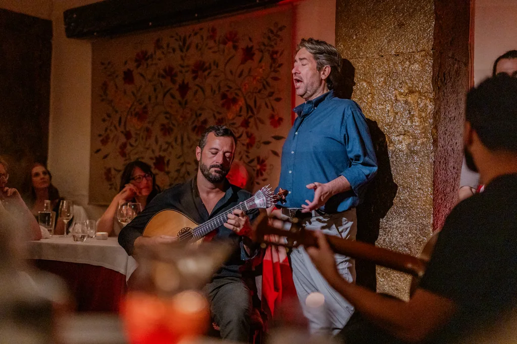 Fado singer performing beneath the floral mural, the guitarist seated
