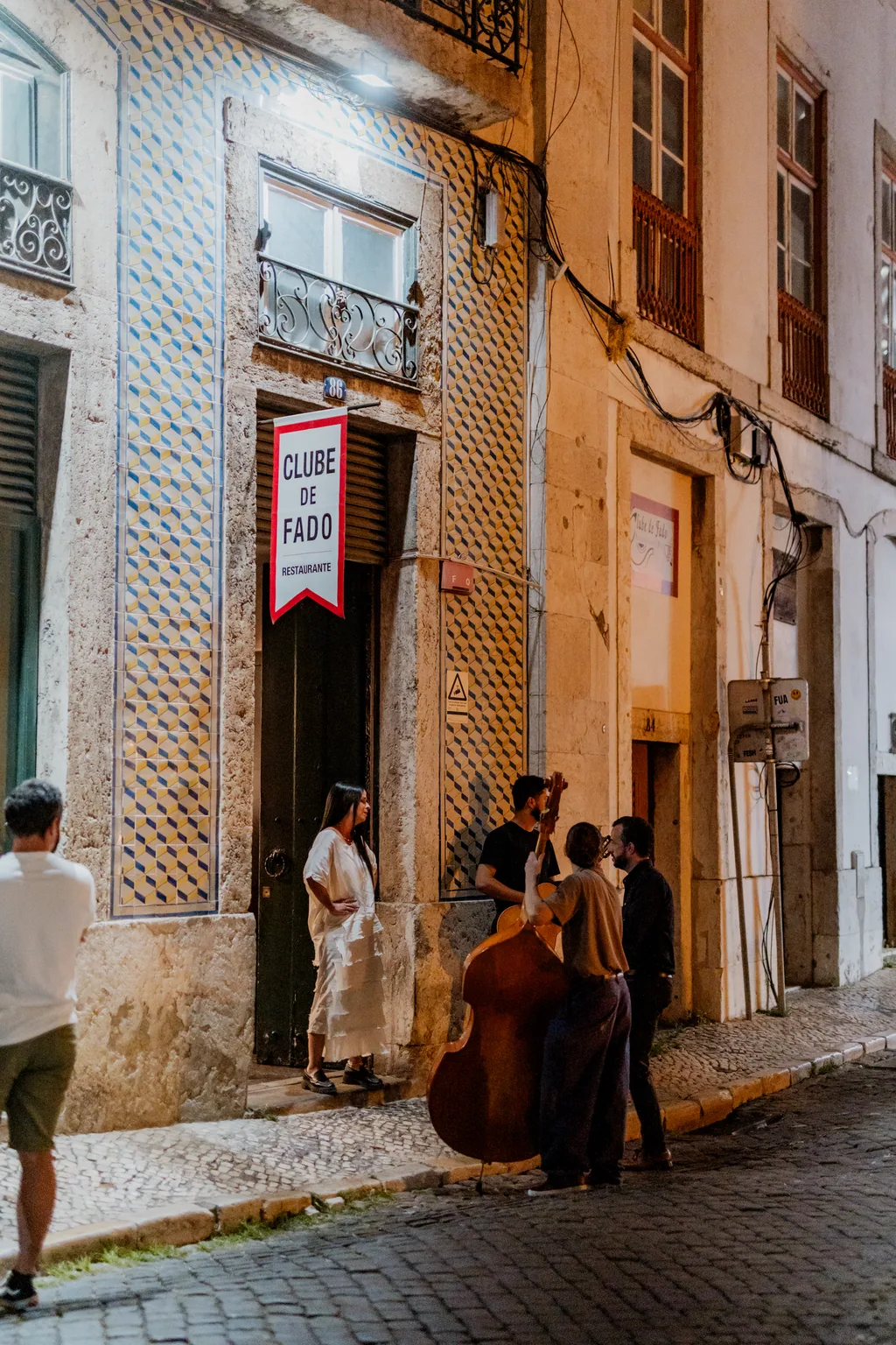 The Clube de Fado banner in the street, musicians against the wall